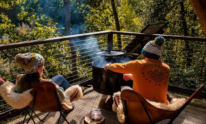 Couple cooking on a firepit on a deck of glamping accommodation at Hay-on-Wye, Wales